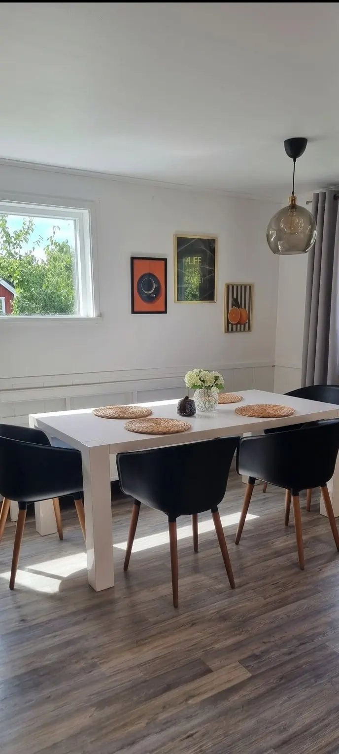 Dining area with a white table and black chairs by a window facing the garden