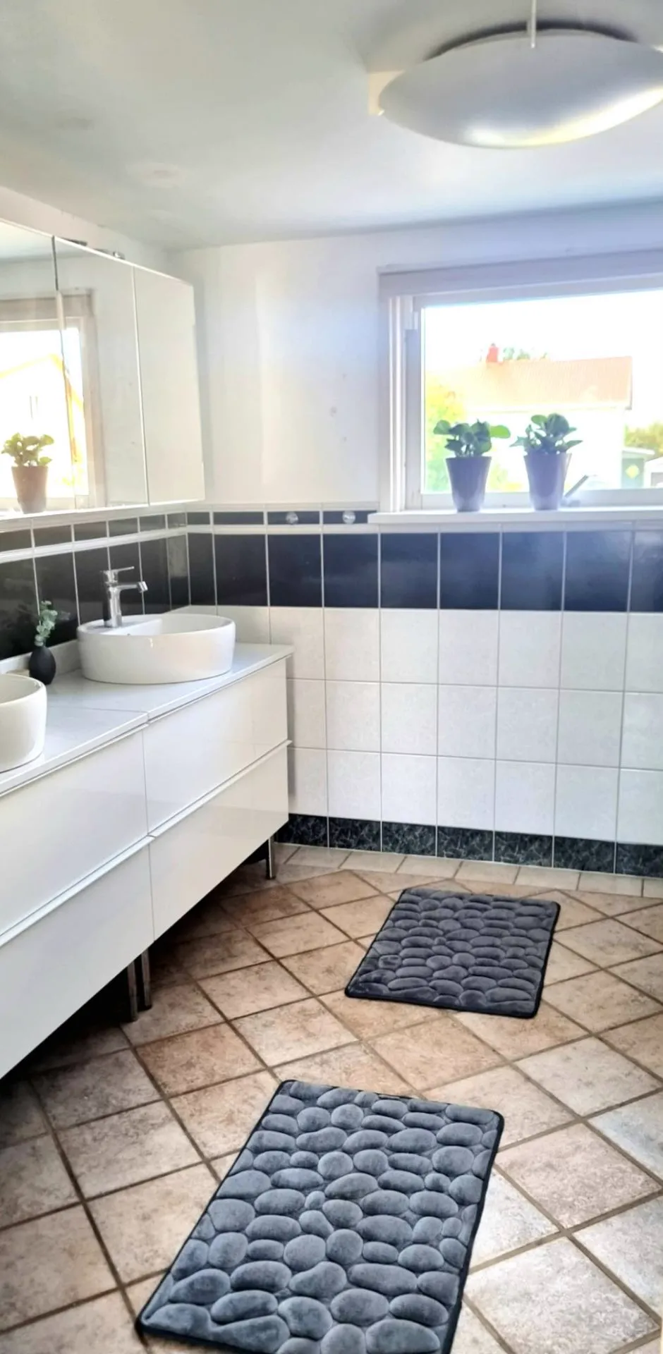 Bathroom with two washbasins on a white vanity, dark blue tiled wall and a window with plants