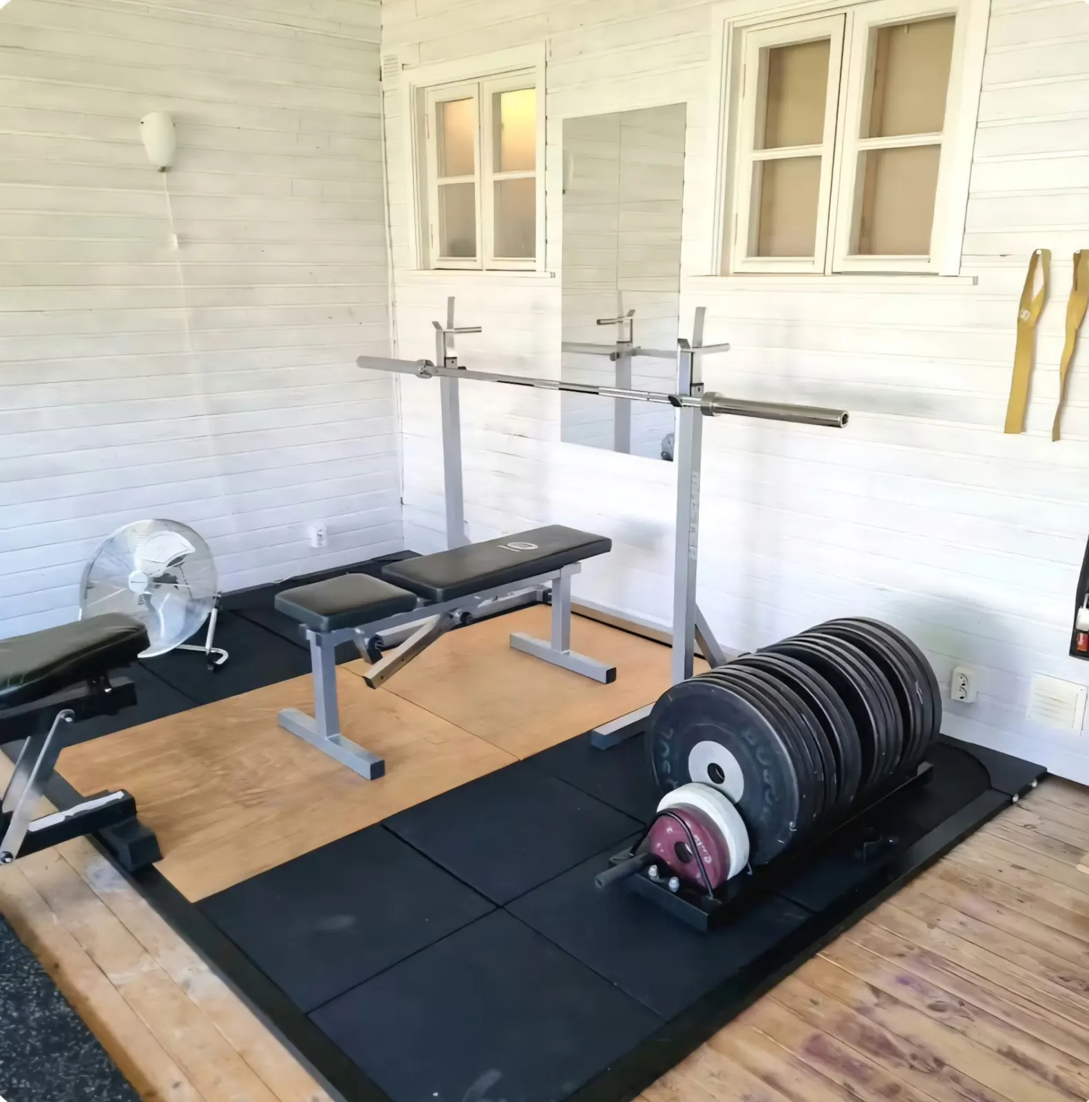 The house gym with a barbell on a rack, adjustable bench and weight plates