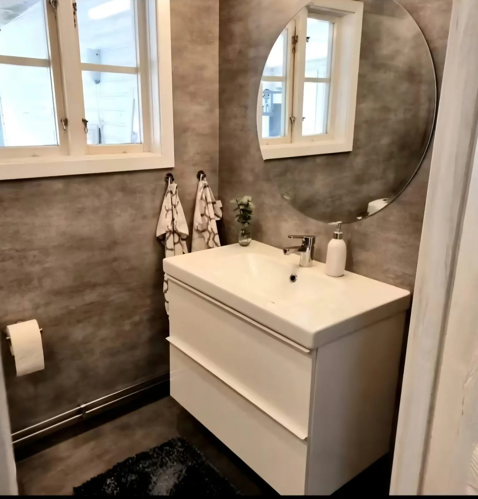 Bathroom with concrete walls, white washbasin and round mirror